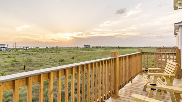 A wooden deck with a view of a grassy landscape and distant structures. - Sunset Bellini - Hot Tub, Golf Cart, Dog Friendly! (Bolivar Peninsula)