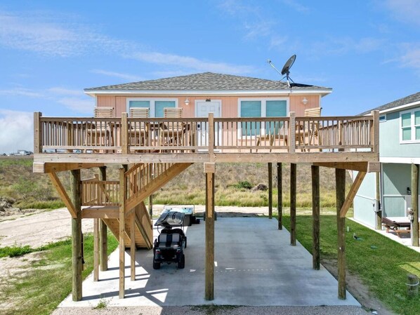 A two-story house with a deck, a satellite dish, and a vehicle in the driveway. - Sunset Bellini - Hot Tub, Golf Cart, Dog Friendly! (Bolivar Peninsula)