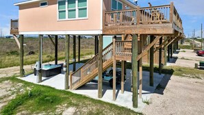 A two-story wooden structure with a balcony, a hot tub, and a deck. - Sunset Bellini - Hot Tub, Golf Cart, Dog Friendly! (Bolivar Peninsula)
