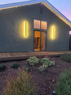 A modern building with a sloped roof, a wooden deck, and a well-maintained garden with various plants. - Detached Guest House (Los Altos Hills)