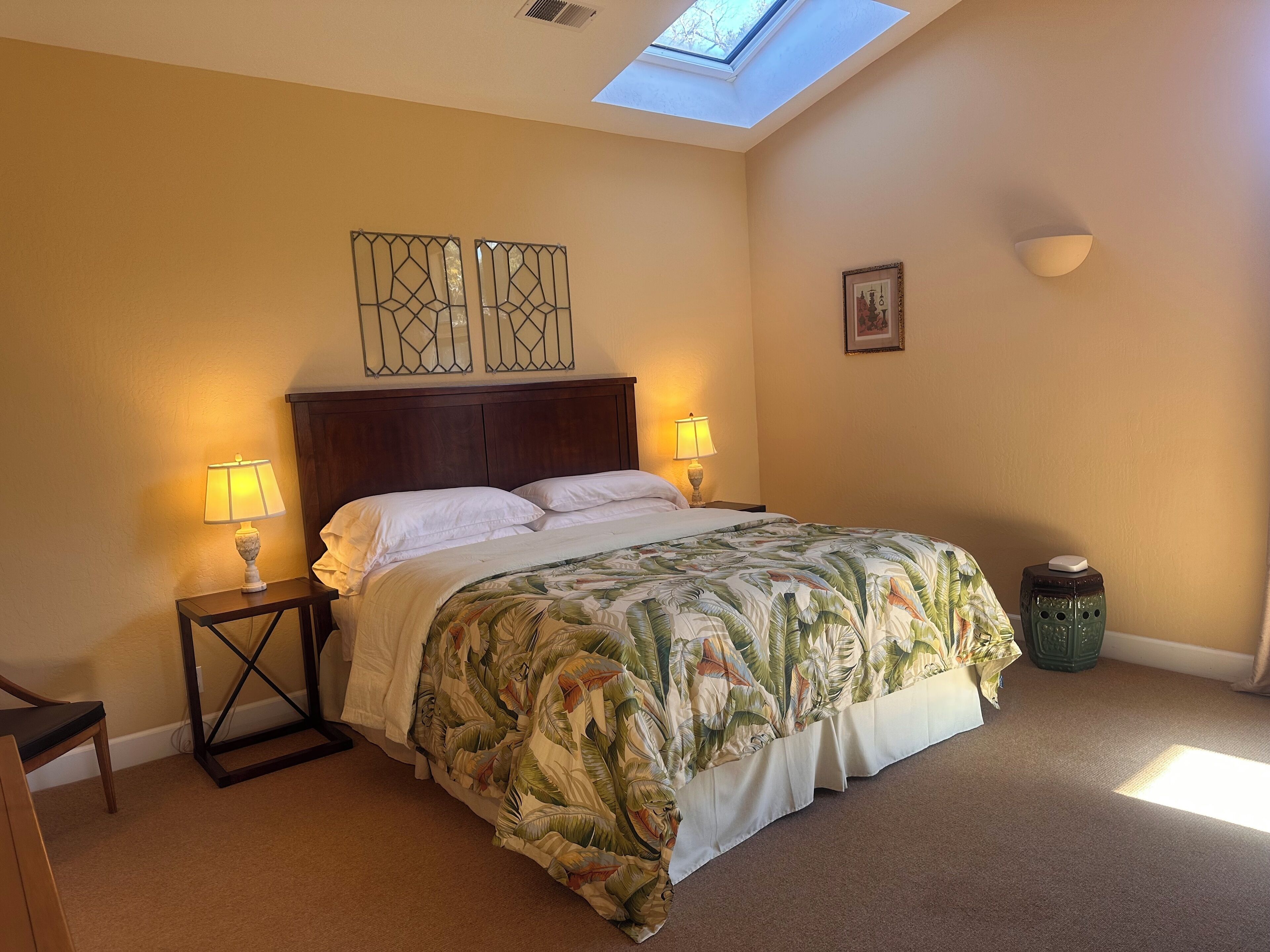 Une chambre à coucher comprenant un lit, deux lampes de chevet, une table de chevet, une petite table, un élément décoratif mural et un puits de lumière.