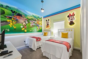 Een kinderkamer met twee bedden, een muurschildering, Mickey Mouse kunst aan de muur en een bureau met een televisie.