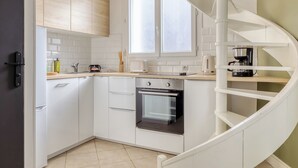 A modern kitchen with white cabinetry, a built-in oven, a coffee maker, and a spiral staircase. - Louis, maison de ville en copro (Rouen)