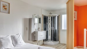 A hotel room with a bed, a walk-in closet, a shower enclosure, and an orange accent wall. - Louis, maison de ville en copro (Rouen)