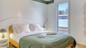 A bedroom with a bed, bedside lamps, a green bedspread, and a view of the outside. - Les Mathurins, F2 unique terrasse, parking et sport (Rouen)