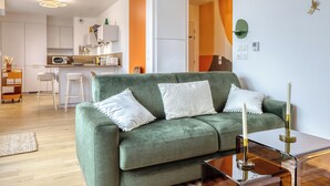 A modern living room with a green sofa, white cushions, and a glass coffee table. - Les Mathurins, F2 unique terrasse, parking et sport (Rouen)