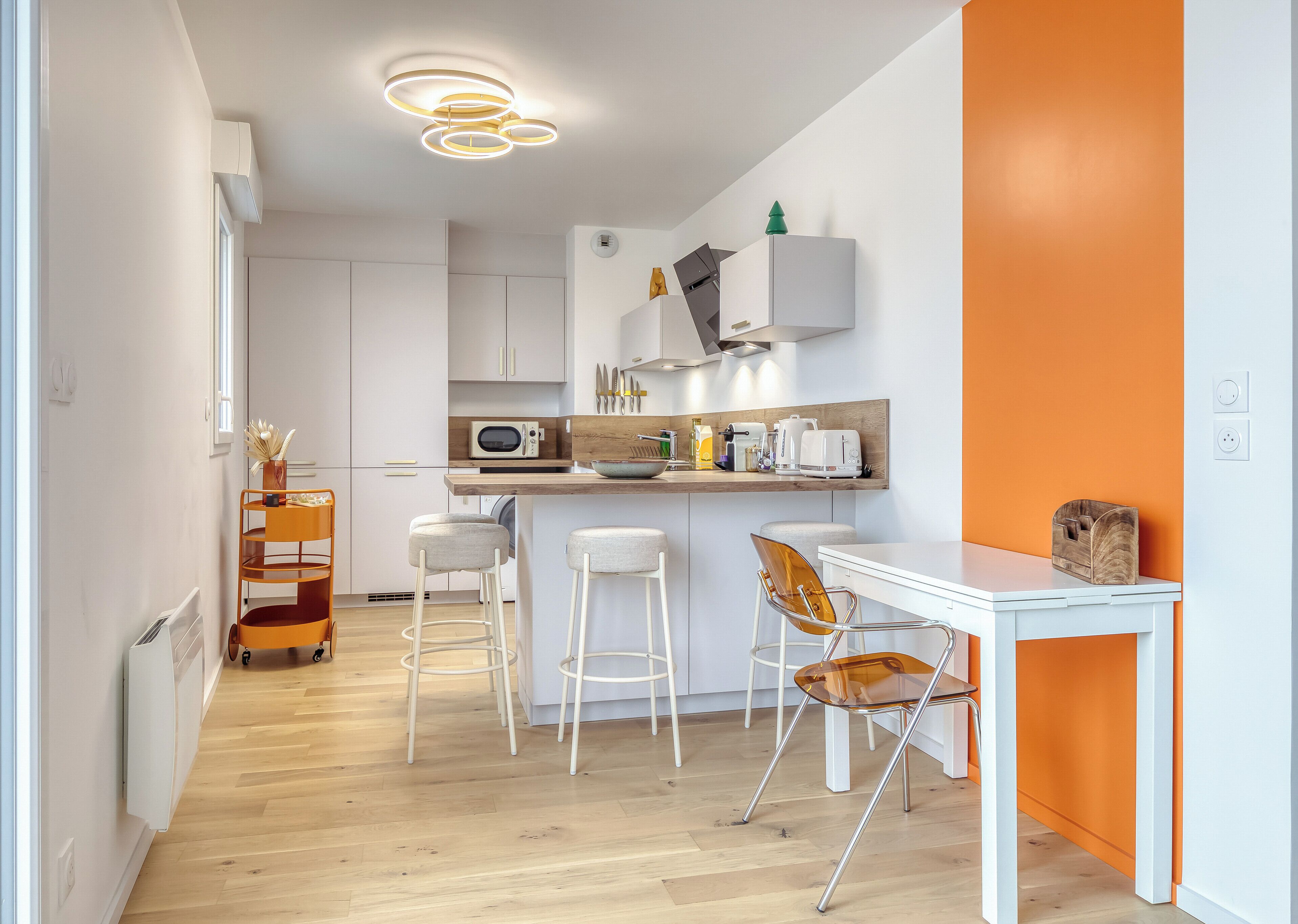 A modern kitchen with white cabinets, a microwave, and a wooden countertop. There are two bar stools and a white dining table with a wooden side table.