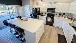 A modern kitchen with white cabinetry, a central island, a microwave, a refrigerator, and a coffee maker. - Tinkerbells Suites, 4m Disney, 6/5.5 Large pool+Spa, 4 themed masters, pets (Kissimmee)