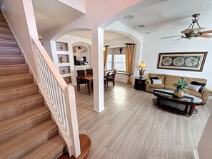 A spacious living area with a wooden staircase, a dining table with chairs, a sofa, and a ceiling fan. - Tinkerbells Suites, 4m Disney, 6/5.5 Large pool+Spa, 4 themed masters, pets (Kissimmee)