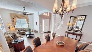 A spacious living room with a large dining table, comfortable seating, and a staircase leading to another level. - Tinkerbells Suites, 4m Disney, 6/5.5 Large pool+Spa, 4 themed masters, pets (Kissimmee)
