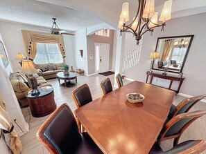 A spacious living room with a large dining table, comfortable seating, and a staircase leading to another level. - Tinkerbells Suites, 4m Disney, 6/5.5 Large pool+Spa, 4 themed masters, pets (Kissimmee)