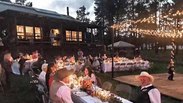 Un área de comedor al aire libre con mesas preparadas para recibir a los huéspedes, rodeada por un edificio rústico y luces colgantes.