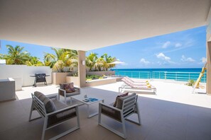 A spacious outdoor patio with a view of the ocean, featuring lounge chairs, a table, and a grill. - Villa Alma Beach Access (Beacon Hill)