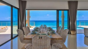 Un comedor con vista al océano, ventanas amplias y mobiliario de mimbre.
