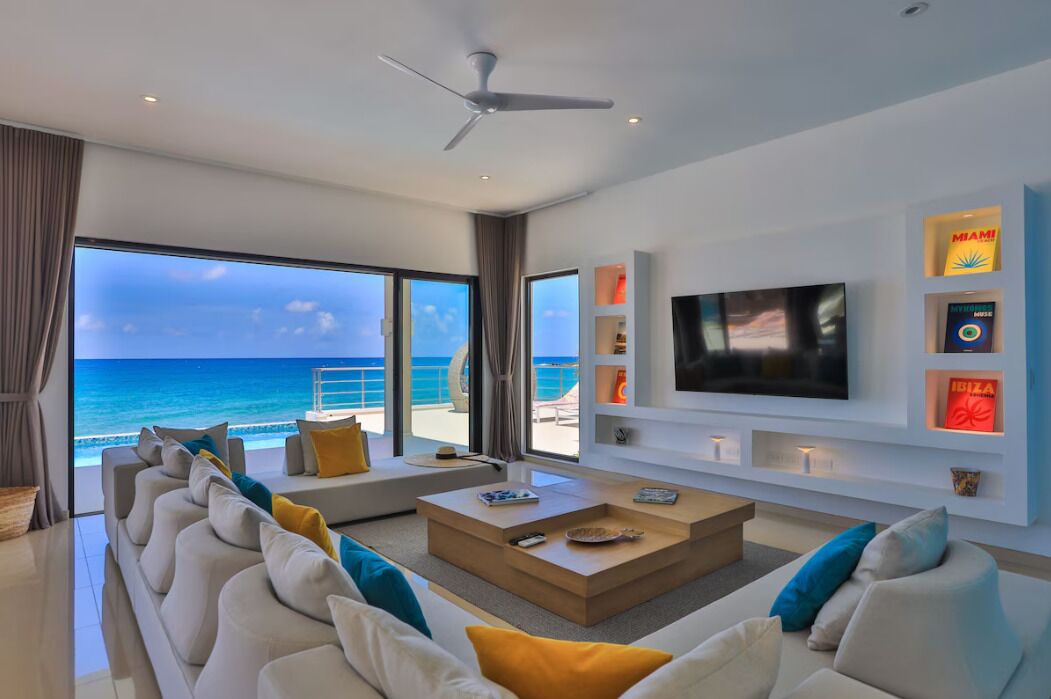 Ein modernes Wohnzimmer mit großem Fernseher, bequemen Sitzmöglichkeiten und Meerblick.