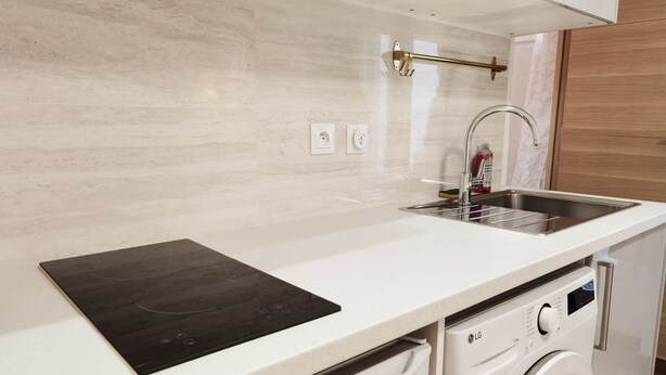 A modern kitchen with a built-in washing machine, a stainless steel sink, and a black induction cooktop. - Modern Bright Studio near Parc de la Villette for2 (Paris)