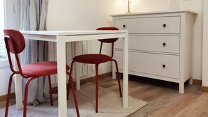 A room with a white table and two red chairs, a white dresser with drawers, a lamp, and a window with curtains. - Modern Bright Studio near Parc de la Villette for2 (Paris)