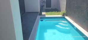 Ein kleiner, rechteckiger Pool mit klarem, blauem Wasser, umgeben von einer gefliesten Terrasse und einer niedrigen Mauer.