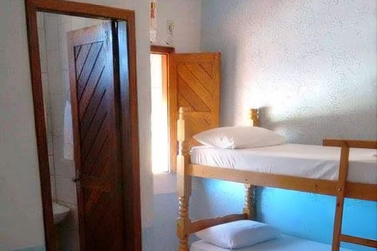 Una habitación con literas, una cama individual, una puerta de madera y suelo de baldosas.
