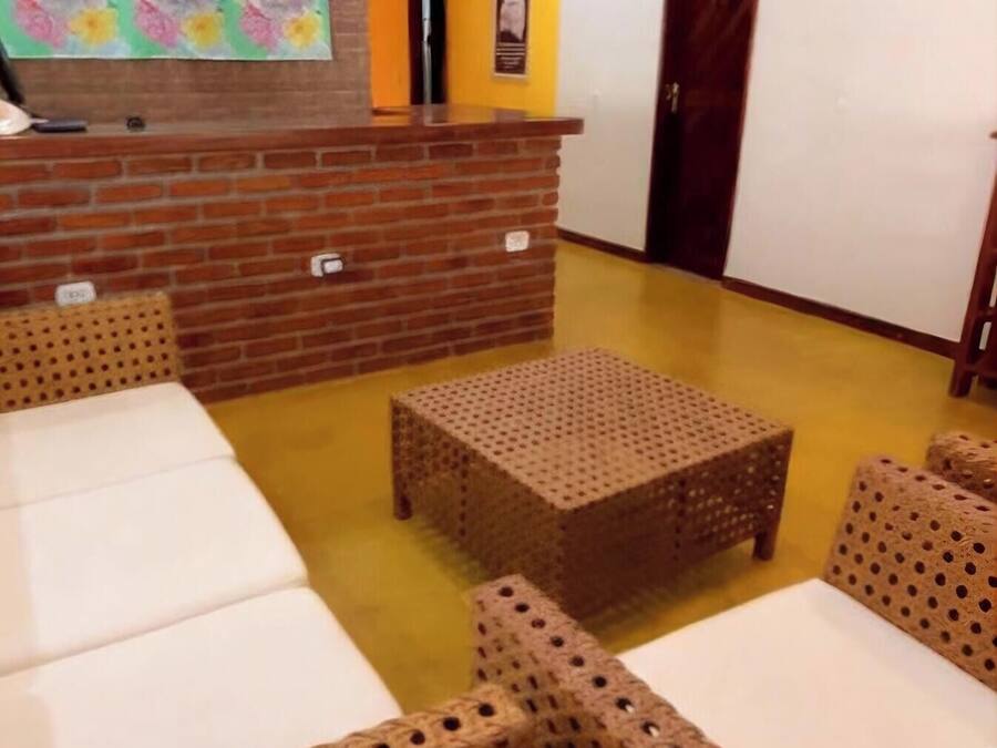 Een kamer met rieten meubels, een accentmuur van baksteen en een kleurrijk bloemen schilderij.