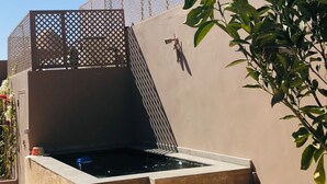 Ein Whirlpool mit einer Holzbank und Stufen, umgeben von einem Zaun und Topfpflanzen.