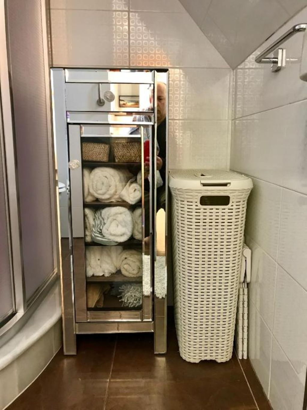 Une salle de bain équipée d’un sèche-serviettes intégré, d’un panier à linge en osier blanc et d’un espace douche.