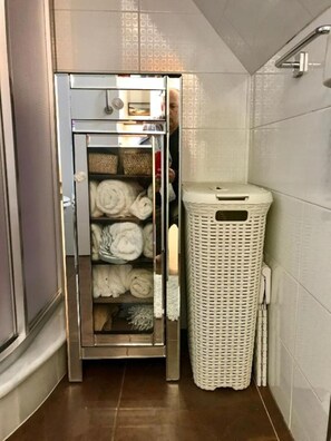 Une salle de bain équipée d’un sèche-serviettes intégré, d’un panier à linge en osier blanc et d’un espace douche.