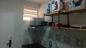 A kitchen with a gas stove, a microwave, and a shelf with kitchen appliances. - Studio Barreto Leme 12 (Campinas)
