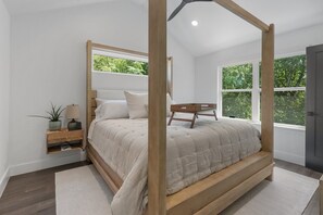A four-poster canopy bed with a wooden frame, a bedside table with a lamp, and a view of greenery through the windows. - 'Welcome to Luxury at its Finest,' Your Private Oasis Awaits. (Austin)