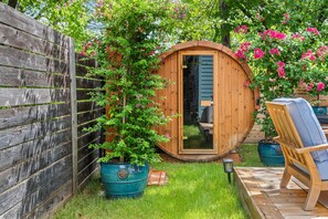 A wooden barrel structure with a door, surrounded by a wooden fence and a garden with a chair and a potted plant. - 'Welcome to Luxury at its Finest,' Your Private Oasis Awaits. (Austin)