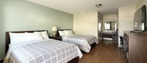 A hotel room with two beds, a desk, a mirror, and a kitchenette.