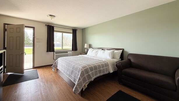 A bedroom with a bed, a sofa, a desk, and a door leading to a balcony.