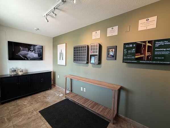 A hotel lobby with a television, air conditioning units, a bench, and informational signs on the wall.