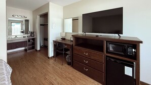 A hotel room with a wooden floor, a desk with drawers, a flat-screen TV, a microwave, and a small refrigerator.