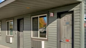 A row of motel rooms with individual doorways and windows, a covered parking area, and a clear sky.