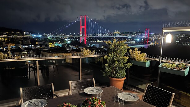 A rooftop dining area with a table set for four, overlooking a cityscape with a prominent bridge. - Ortaköy Suit (İstanbul)