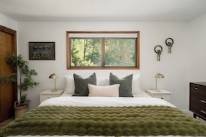 A bedroom with a bed, two nightstands, a window, a painting, and a plant. - Cozy Cabin: Relax in Hot Tub Overlooking Creek (Rhododendron)