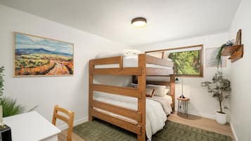 Una cama litera con escritorio y silla, un cuadro, una ventana con vistas y una planta.