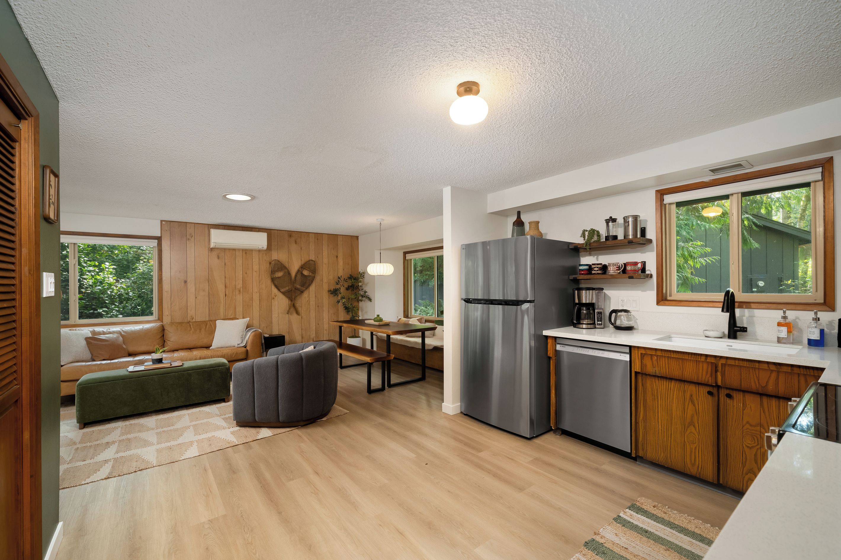A modern kitchen with a stainless steel refrigerator, wooden cabinets, and a window overlooking greenery.