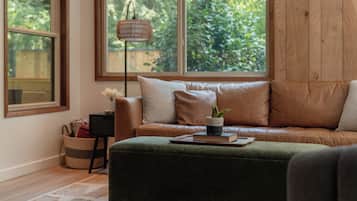A cozy living room with a leather sofa, a green ottoman, and a floor lamp.