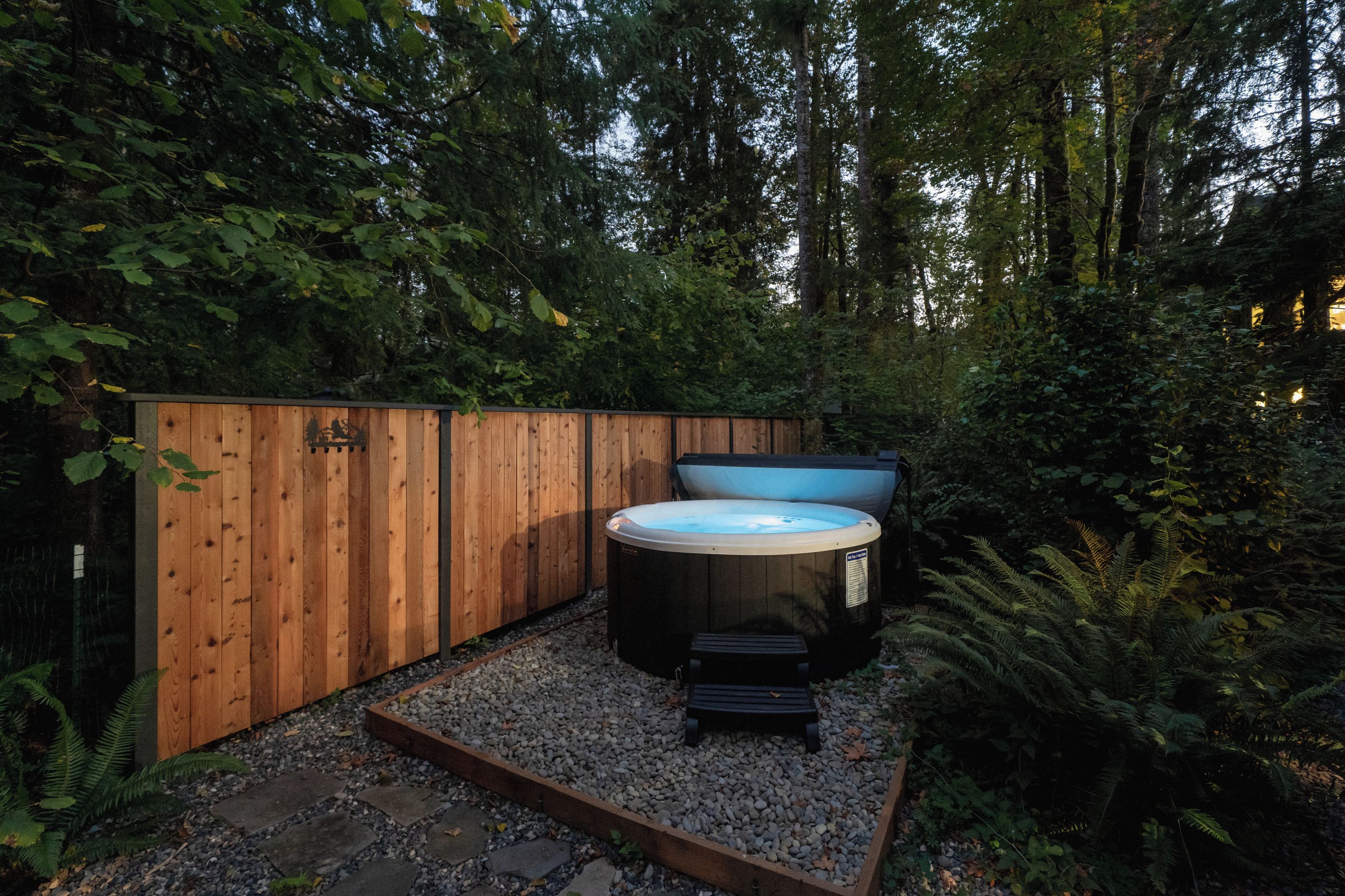 A hot tub and seating area surrounded by a wooden fence and dense foliage.