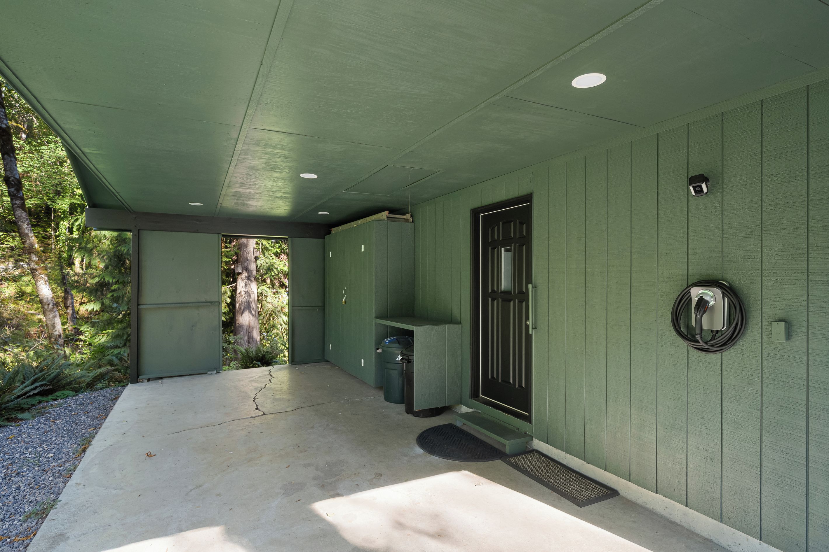 A green-walled building with a concrete porch, a door with a peephole, and a wall-mounted electrical outlet.
