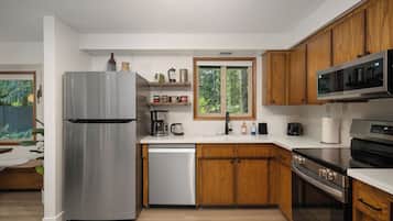 A modern kitchen with stainless steel appliances, wooden cabinets, and a window providing a view of greenery.