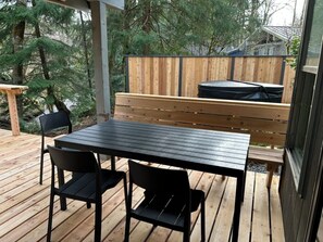 Une terrasse en bois avec une table et des chaises, un banc, et une vue sur des arbres et une maison en arrière-plan.