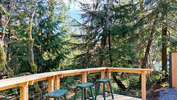 Un pontile in legno con ringhiera, sgabelli verdi e una panca.