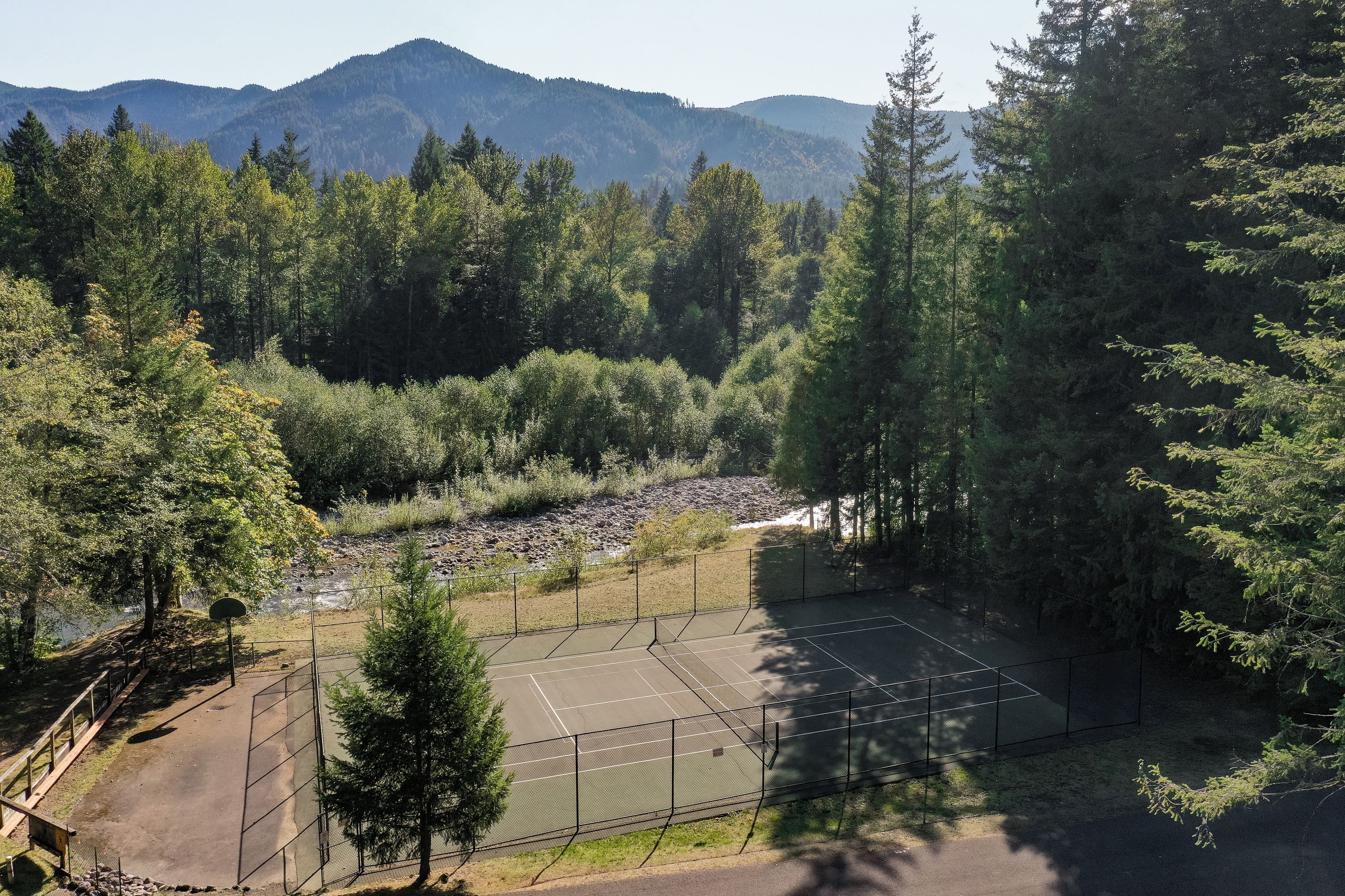 A tennis court surrounded by dense forest and mountains in the background.