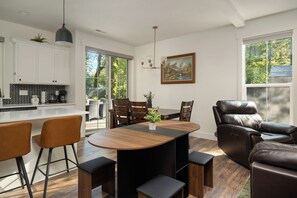 Una cocina moderna con armarios blancos, un comedor con mesa y sillas de madera, y un sillón reclinable de cuero.
