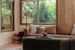 A cozy living room with a leather sofa, a green ottoman, and a floor lamp. - Mt. Hood Hideaway + Creekside Hideaway: Two Homes, Two Hot Tubs, Sleeps 14 (Rhododendron)