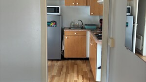 A narrow hallway leading to a kitchen with wooden cabinets, a microwave, a refrigerator, and a sink. - Fully equipped mobile home for 4–6 people in Hourtin, between the lake, the forest, and the ocean🏖️ (Hourtin)