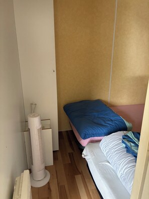 A small, compact room with a bed, a standing heater, and a wooden floor. - Fully equipped mobile home for 4–6 people in Hourtin, between the lake, the forest, and the ocean🏖️ (Hourtin)